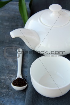 Little white tea cup and a kettle  on grey background