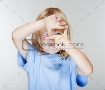 little boy with long blond hair looking through a finger frame - isolated on gray