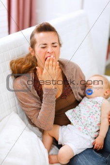 Young mother with sleeping baby on hands yawing
