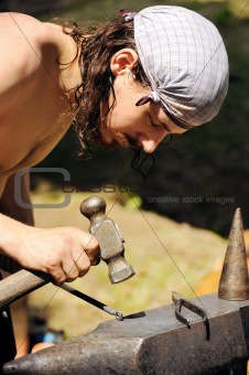 Young blacksmith hammering hot iron on anvil