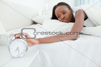 Tired woman switching off her alarm clock