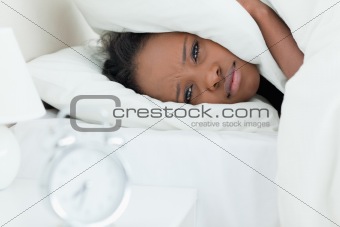 Woman covering her ears while her alarm clock is ringing