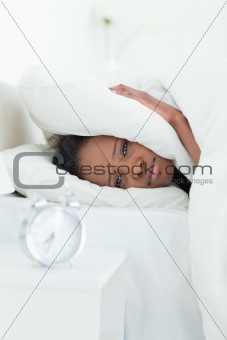 Portrait of a woman covering her ears while her alarm clock is ringing