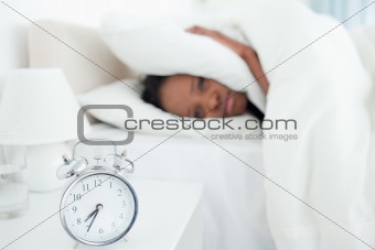 Exhausted woman covering her ears while her alarm clock is ringing