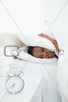 Portrait of a young woman covering her ears while her alarm clock is ringing