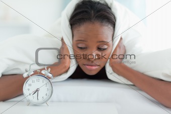 Tired woman covering her ears with a duvet