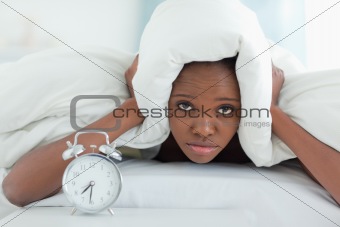 Exhausted woman covering her ears with a duvet