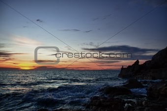 Sunset, rocks and fisherman on sea