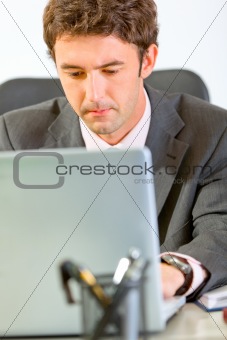 Portrait of modern businessman sitting at office desk and working on laptop
