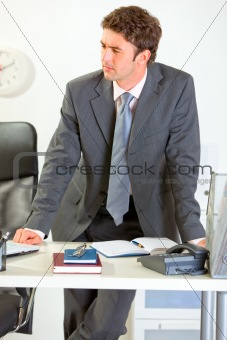 Confident modern businessman holding standing near office desk and looking in corner
