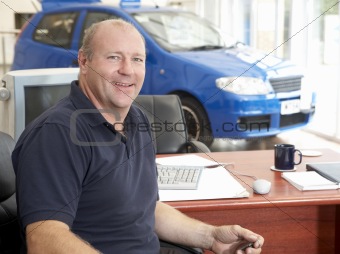 Car salesman sitting in showroom smiling