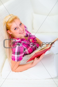 Smiling pretty woman relaxing on sofa and reading book
