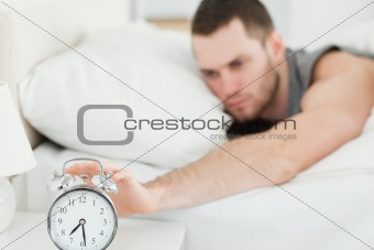 Tired man switching off his alarm clock