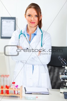 Portrait of doctor woman with crossed arms standing at office desk
