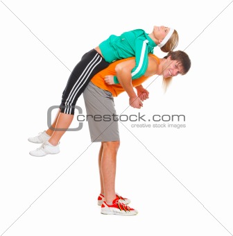 Handsome young man taking slim girl in sportswear on his back isolated on white
