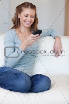 Smiling female surfing the web with her smartphone on the sofa