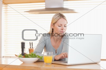 Woman with salad and orange working on laptop in the kitchen
