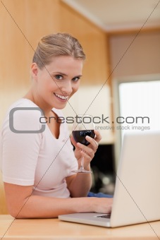 Portrait of a woman using a laptop while drinking red wine