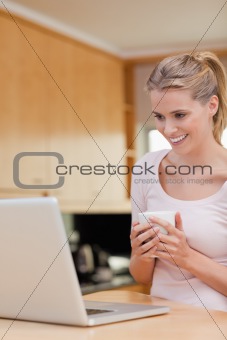 Portrait of a young woman using a laptop while drinking coffee