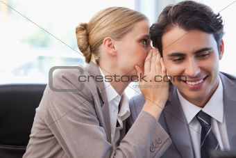 Young businesswoman whispering something to her colleague