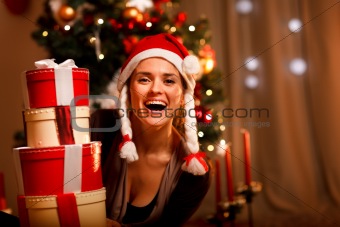 Portrait of laughing woman near Christmas tree looking out from pile of present boxes 
