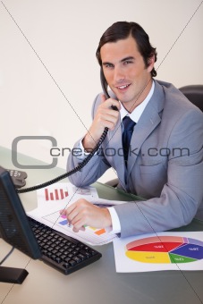 Smiling businessman on the phone working on statistics