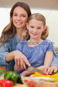 Portrait of a woman slicing bell pepper with her daughter