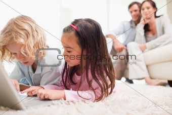 Children using a notebook while their parents are in the background