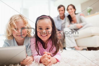 Siblings using a tablet computer while their parents are in the background
