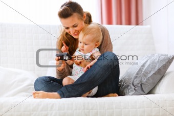 Young mom showing her interested baby photos on camera
