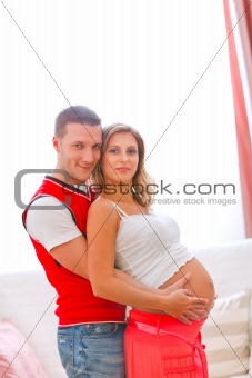 Portrait of young pregnant woman with husband hugging her tummy
