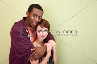 Mixed race teen couple lovingly hug in front of green wall