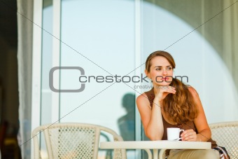 Thoughtful woman sitting on terrace and having cup of coffee
