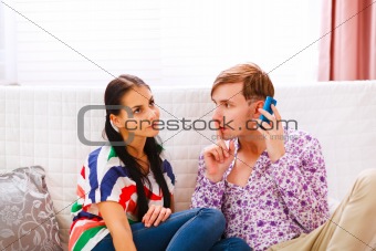 Young man showing shh... gesture to girlfriend while answering mobile phone
