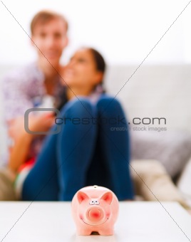 Piggy bank on table and happy young couple in background
