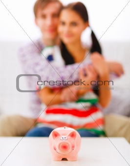 Piggy bank on table and happy young couple in background
