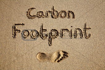 Carbon footprint written in sand on a beach.