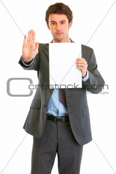 Serious modern businessman holding blank paper and showing stop gesture
