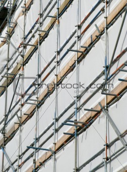 Close up building covered by scaffolding and white tarpaulin.