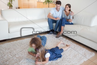 Children using a tablet computer while their happy parents are watching