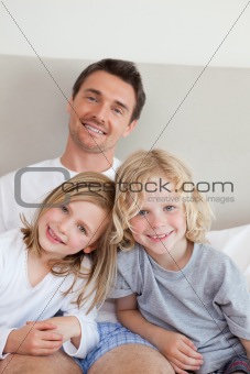 Smiling father sitting on the bed with his children