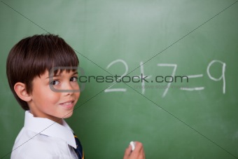 Smiling schoolboy writing an addition