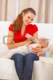 Happy mother sitting on couch and feeding baby