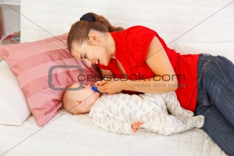 Happy mother laying on couch and giving soother to baby