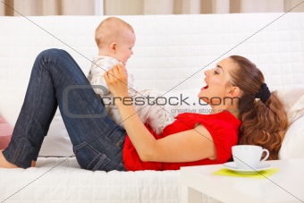 Smiling mother and cute baby playing on divan