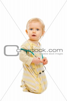 Confused baby with stethoscope sitting on floor isolated on white