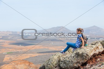 girl sitting on cliff's edge, looking to a sky