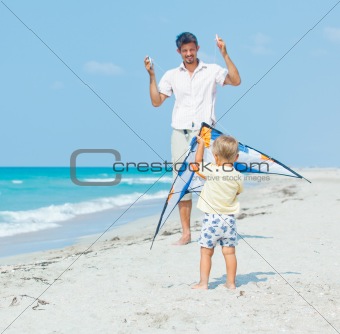 boy with father on beach playing with a kite
