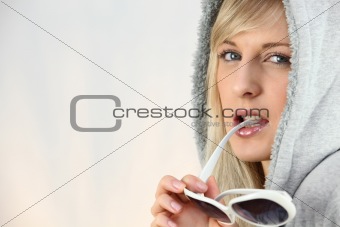 Woman with a hood on and chewing on her sunglasses