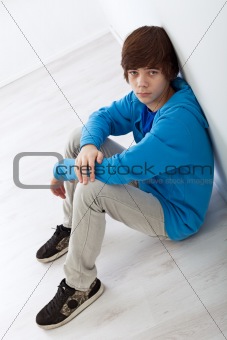 Teenager boy sitting on the floor by the wall
